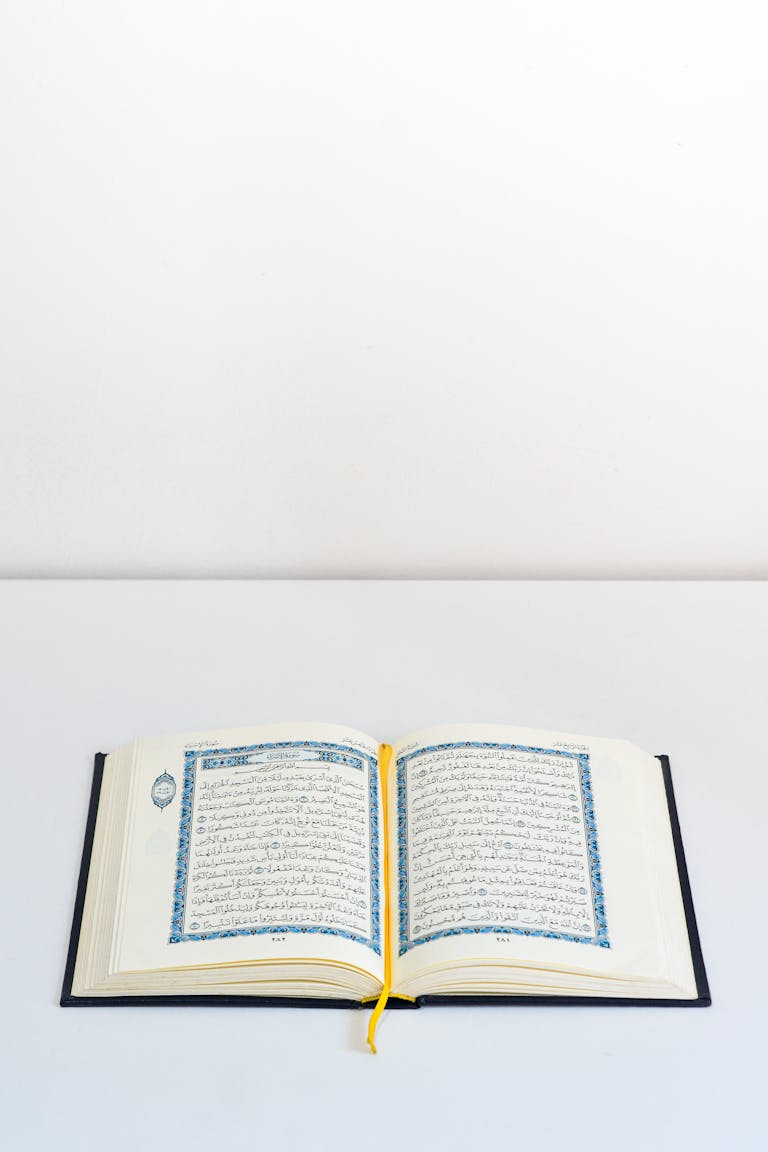 An open Quran on a white table with a yellow bookmark, photographed in a studio setting.
